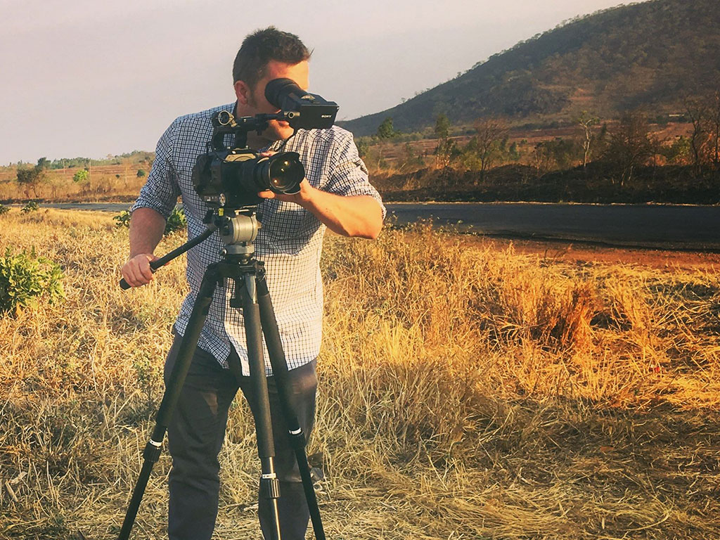 Camera operator standing behind a camera on a tripod